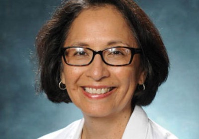 Portrait of Ana Maria López in a lab coat in front of a blue background