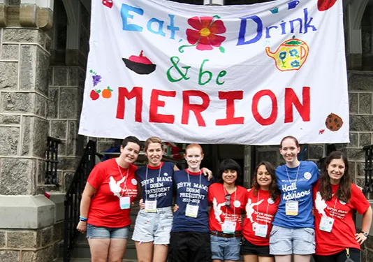 Customs People standing outside of Merion Hall with a banner behind them