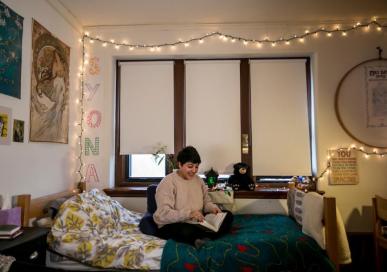 Student sitting on bed in dorm room