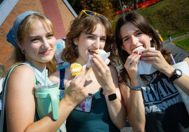 Three students eating cupcakes pose for the camera mid-bite