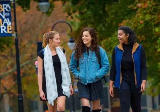 Three students walking on campus with a Bryn Mawr College flag in the background