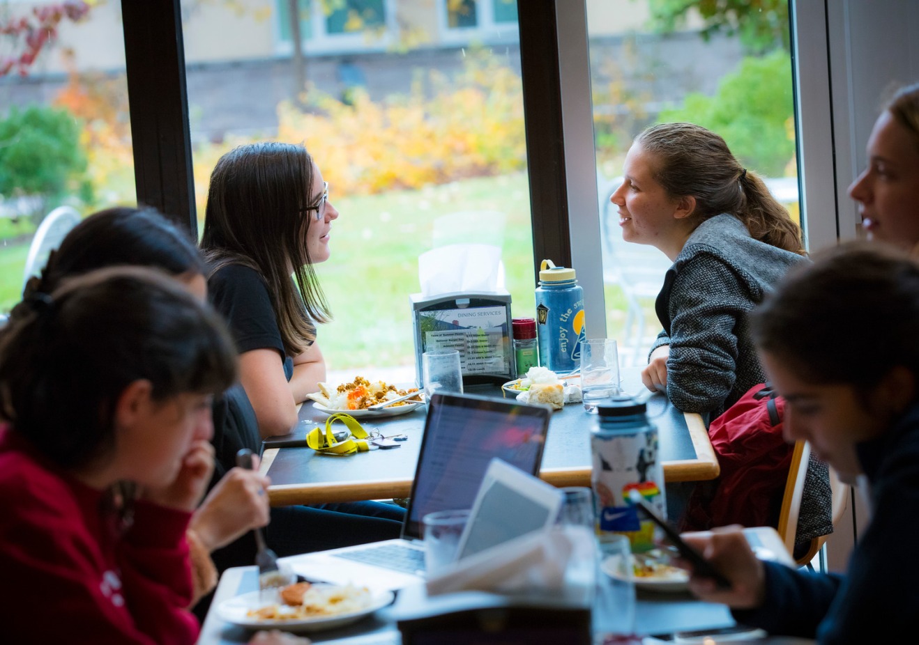 Two students at a table with other students sitting at nearby tables