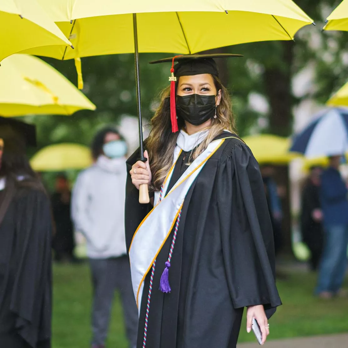 Students walk to graduation with yellow umbrellas