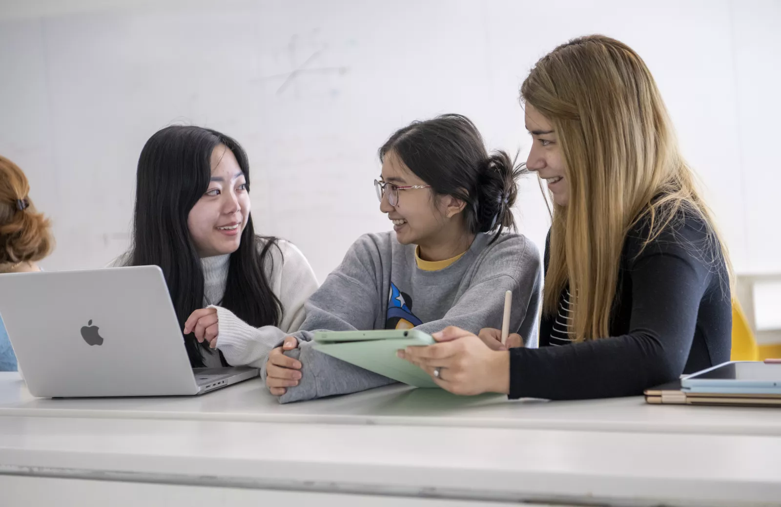 Students smiling at each other while holding a laptop and iPad 