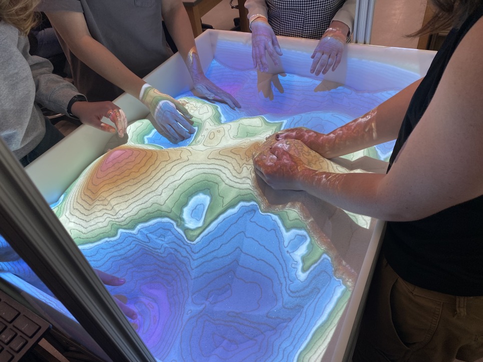 An up close view of students using the digital sandbox, moving the sand around and changing the digital map projected on top of the sand