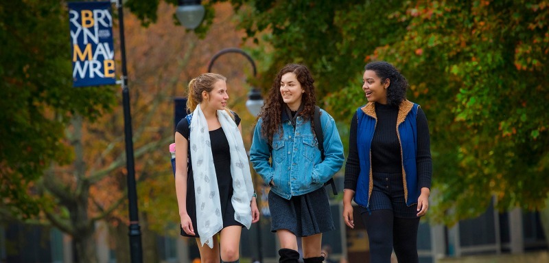 Three students walking on campus with a Bryn Mawr College flag in the background