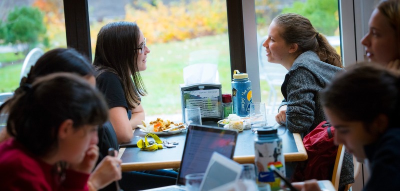 Two students at a table with other students sitting at nearby tables