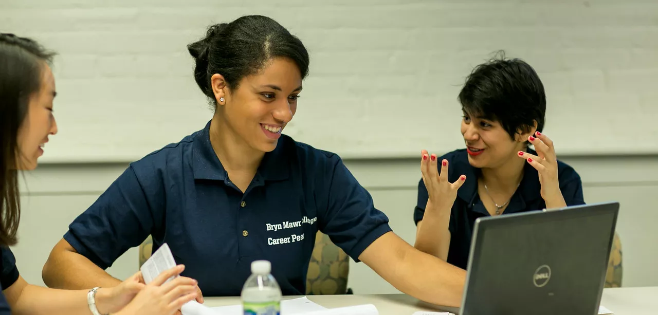 Three students sit at a table looking at a screen.