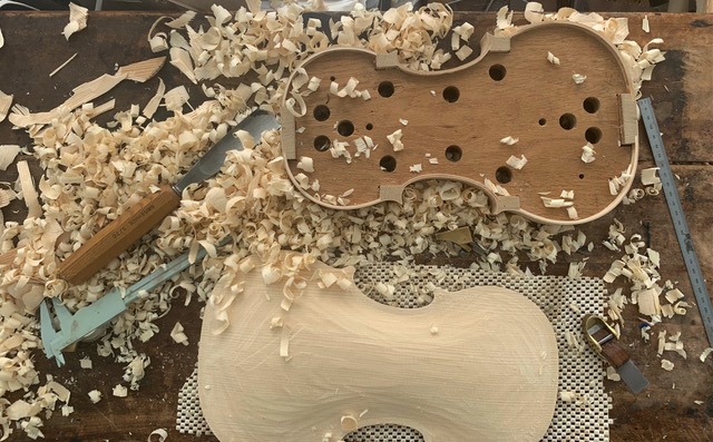 A violin in progress, covered with wood shavings.