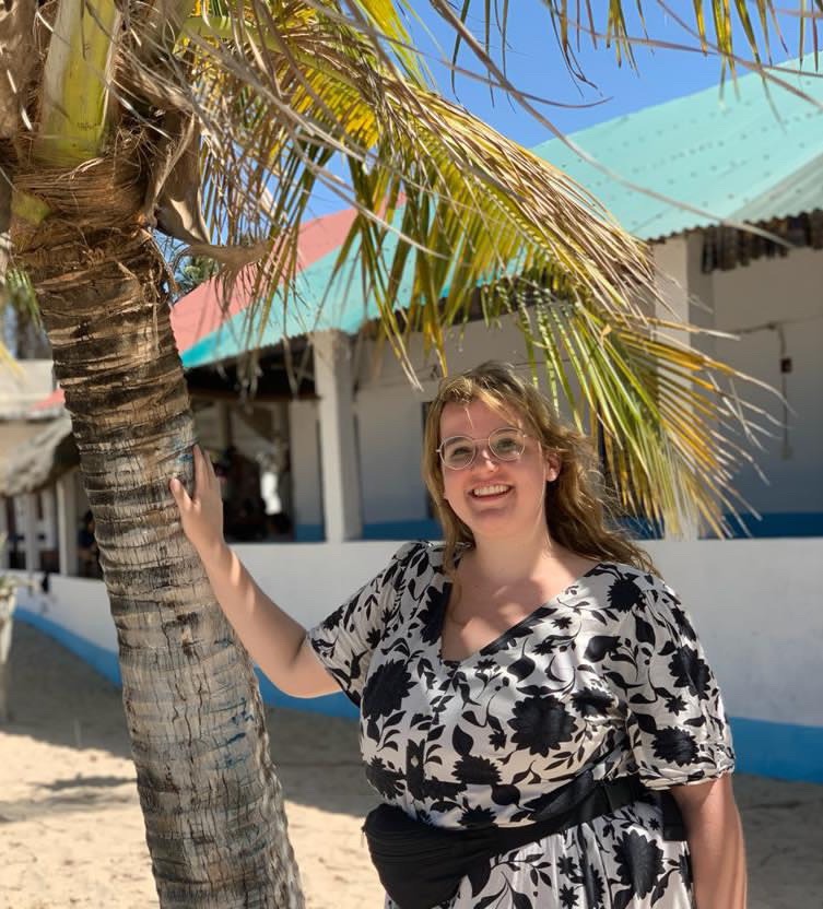 Saskia Holman leaning against a palm tree and smiling at the camera