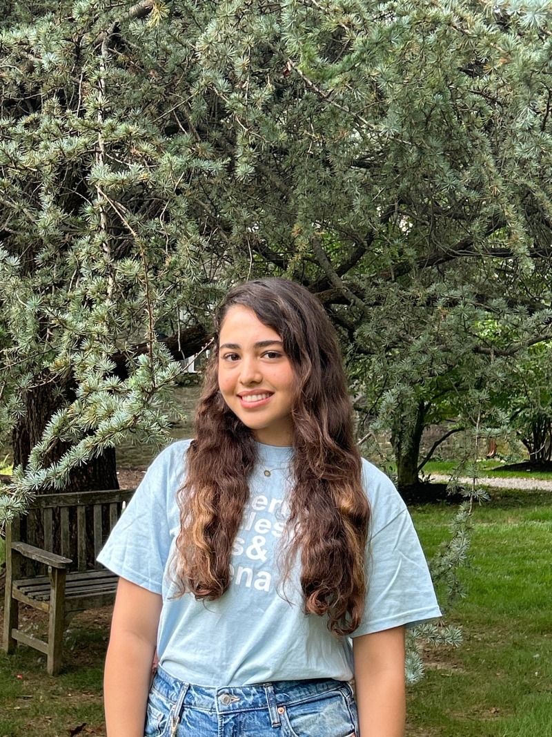 Girl wearing a blue shirt and smiling in front of a tree.