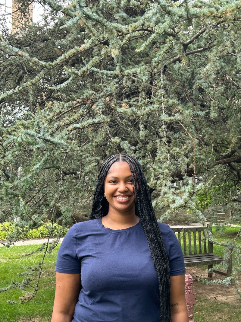 Girl wearing navy blue shirt and smiling in front of trees.