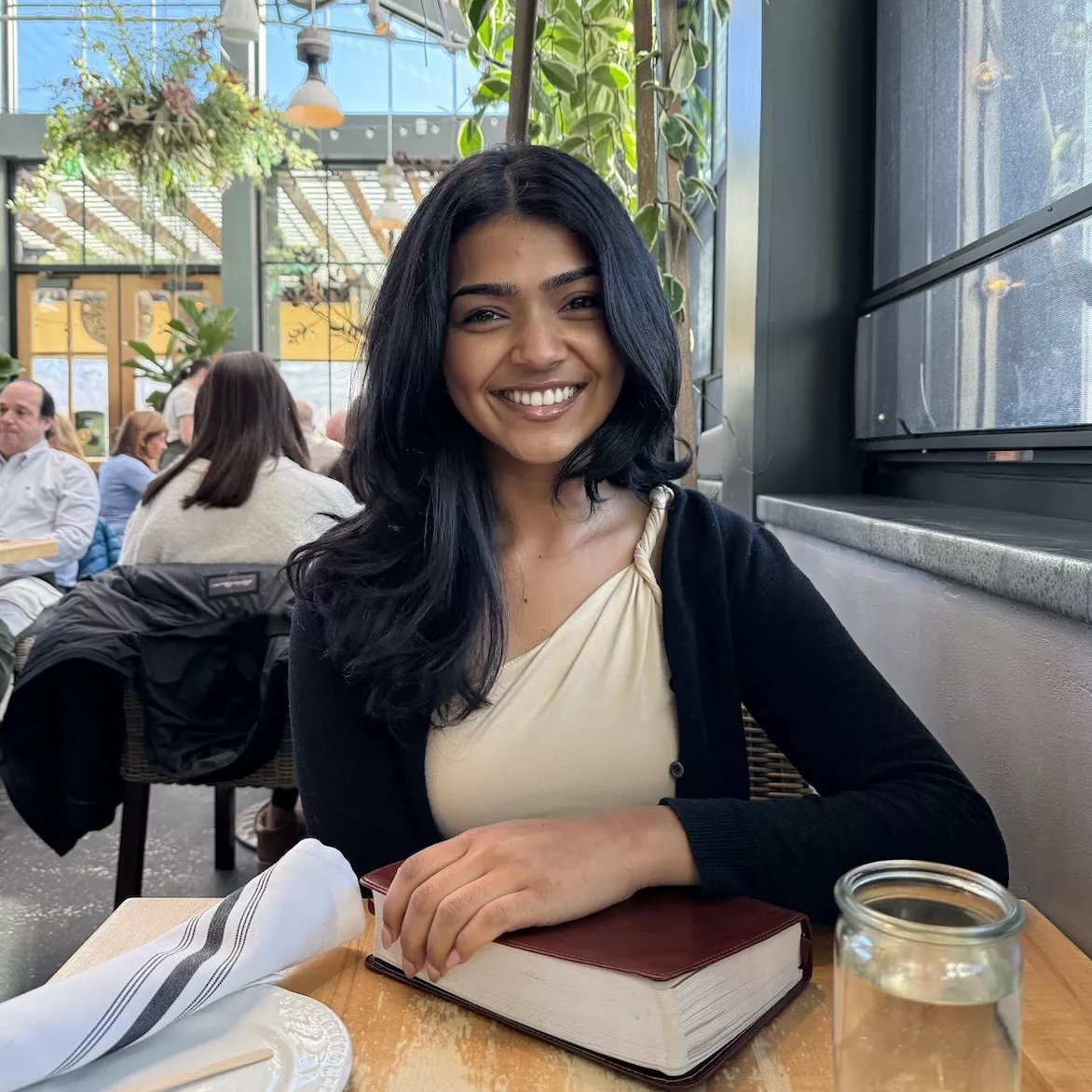 Daniella Jacobs smiling at a cafe table, resting her arms on a book