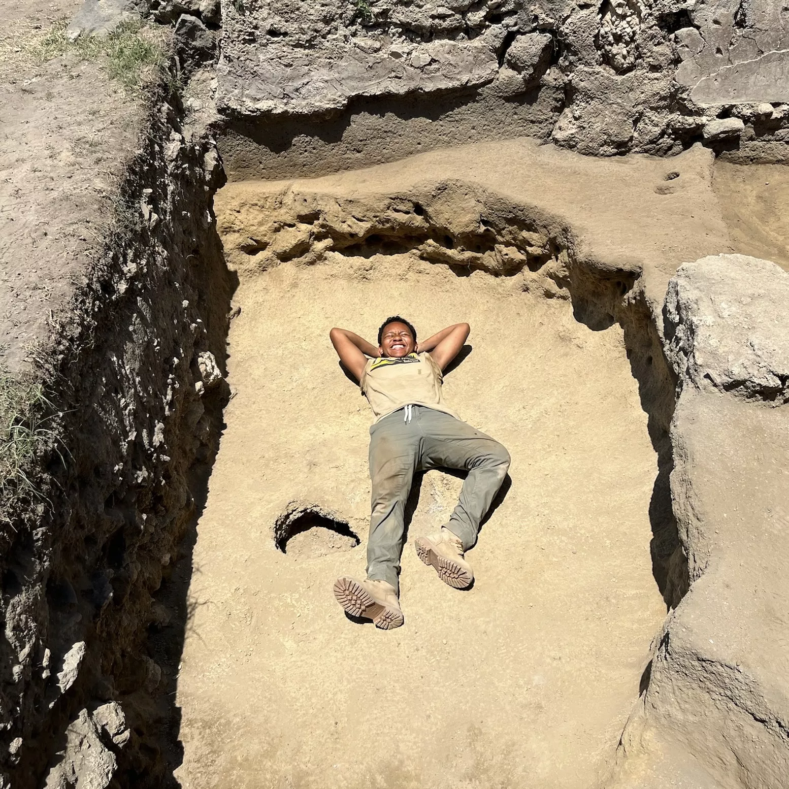 Jasmine Marshall smiling and laying in a dusty pit on an archaeological dig.