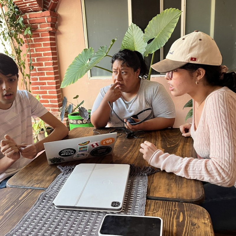 Esenia Baneulos sitting at a table with a Haverford student and a woman. They're chatting and looking at a computer