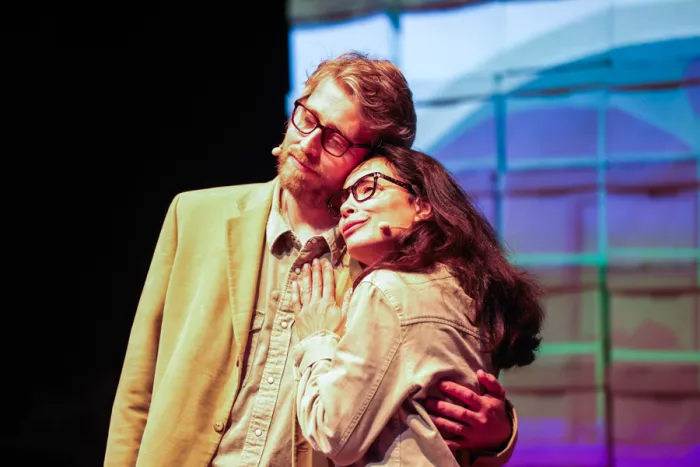 Two actors embrace in front of colorful screen