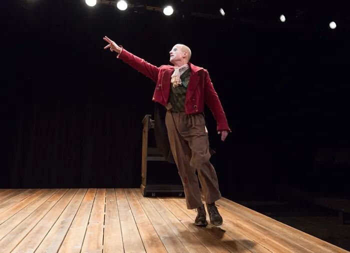 A single actor on a stage in a red jacket